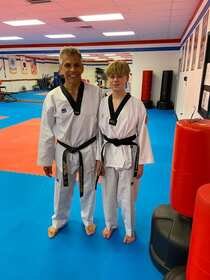 Master Sebastian Gonzalez in his black-belt uniform smiling beside a teen black belt student in the dojang